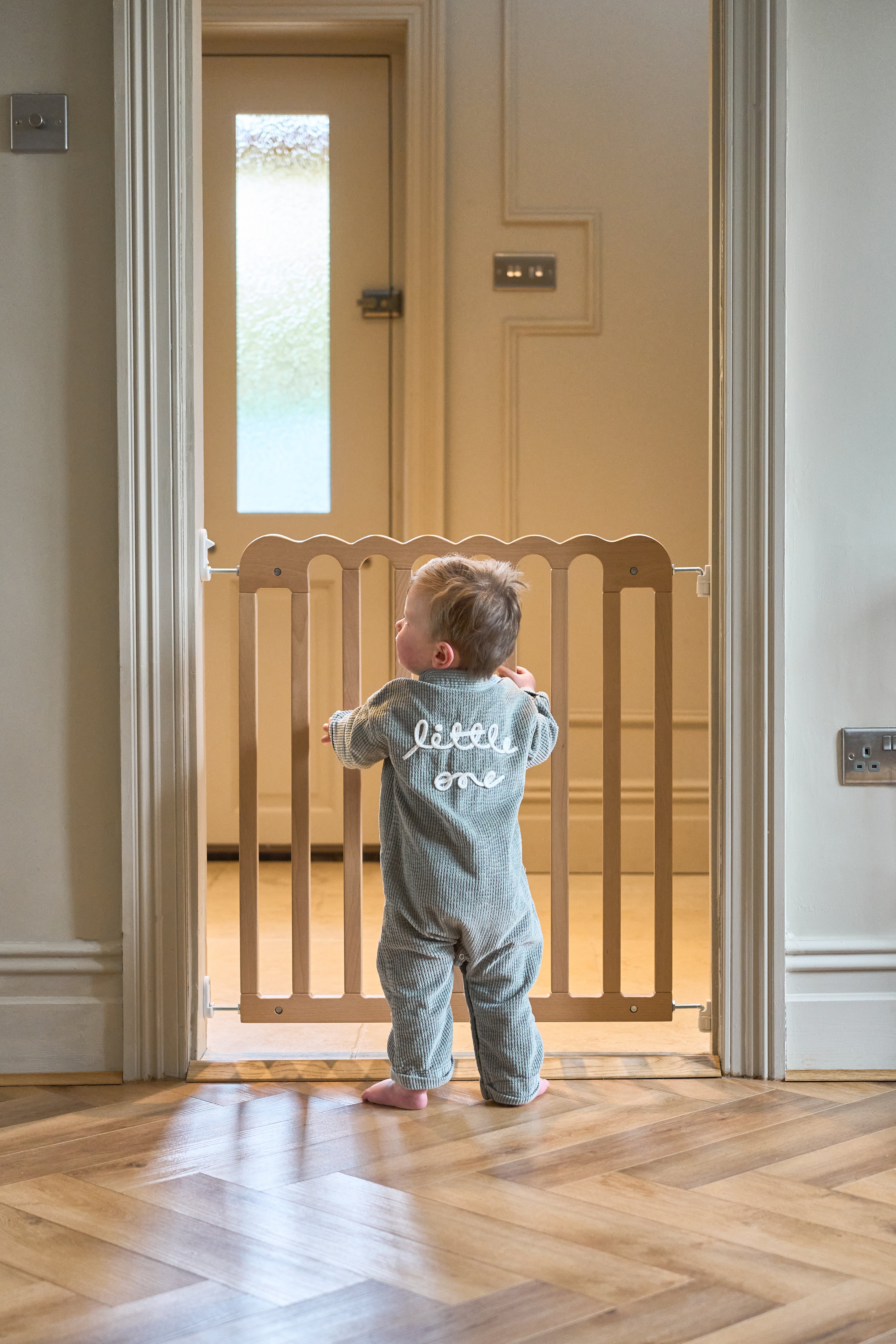 Child standing in a doorway with a wooden baby gate