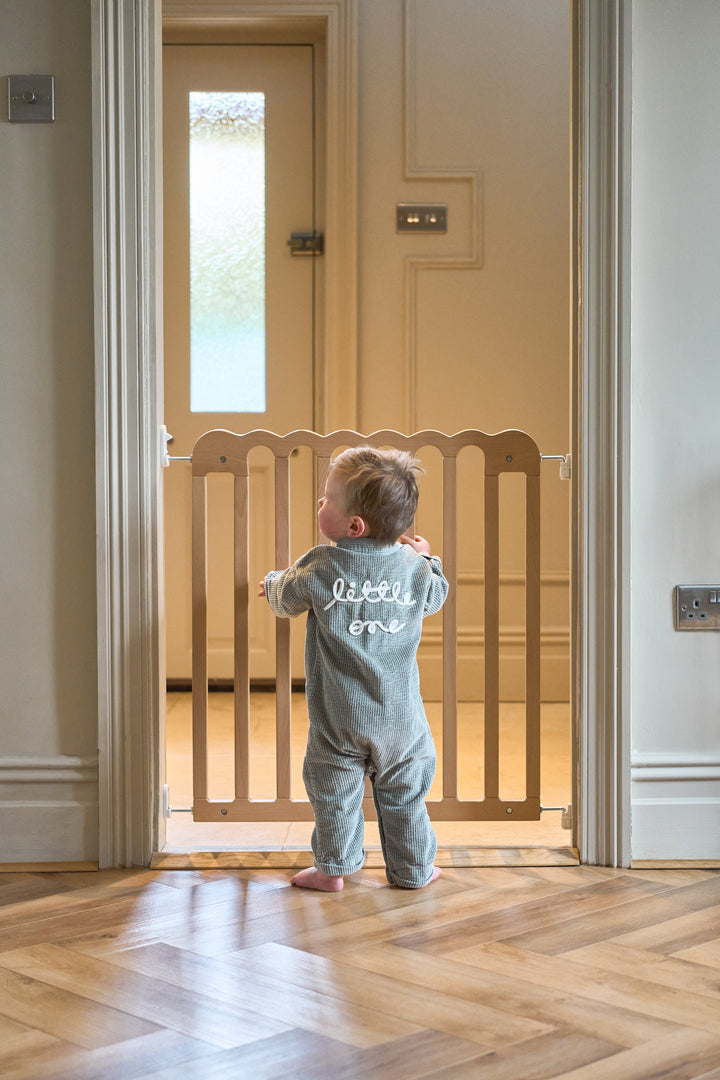 Child standing in a doorway with a wooden baby gate