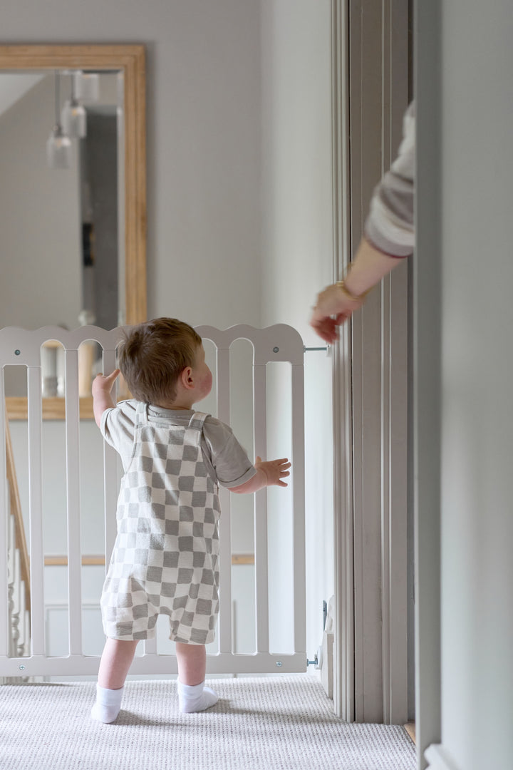 Baby standing next to a baby gate. Aesthetically pleasing baby gate.