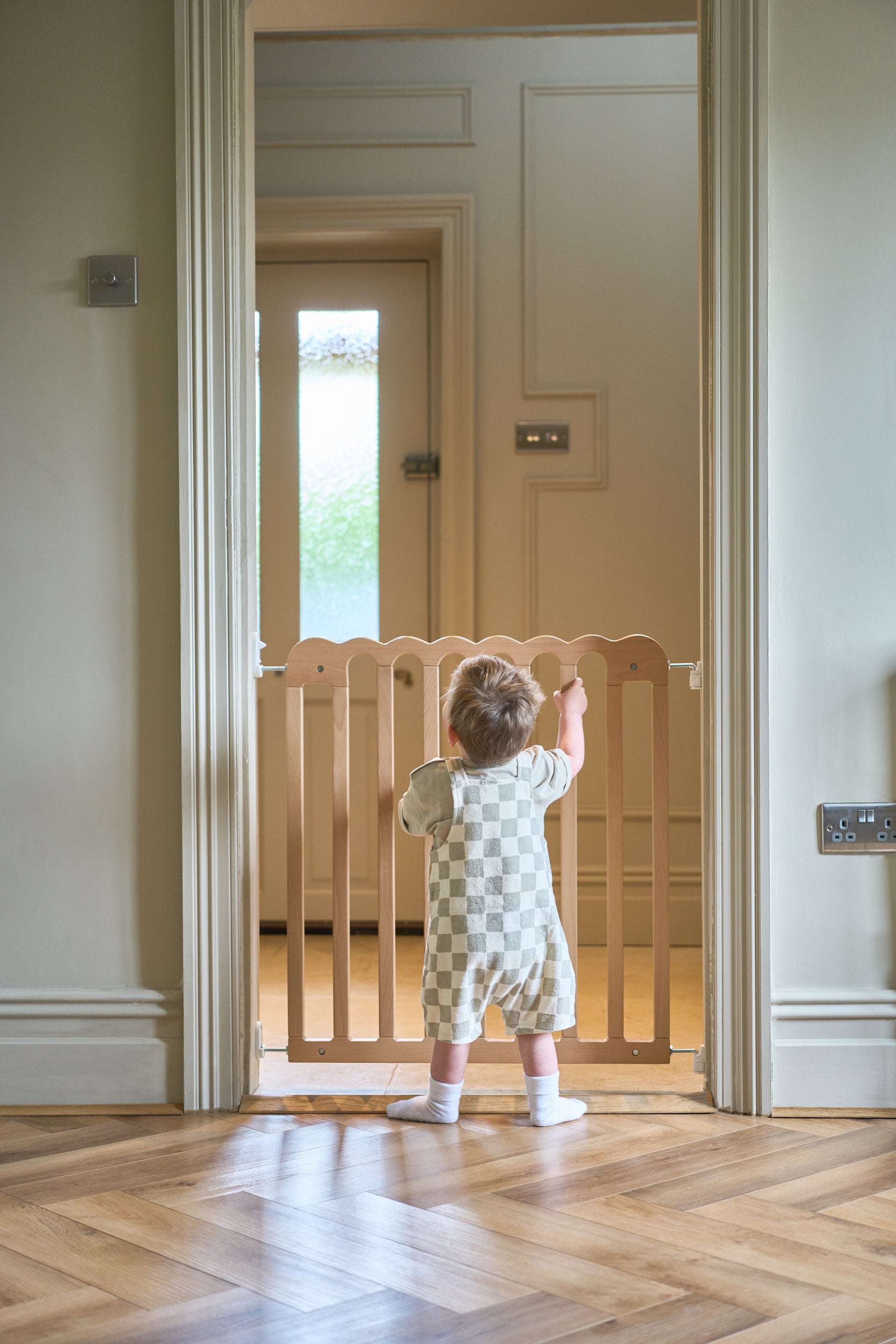 Child standing at a scalloped baby gate in a home setting