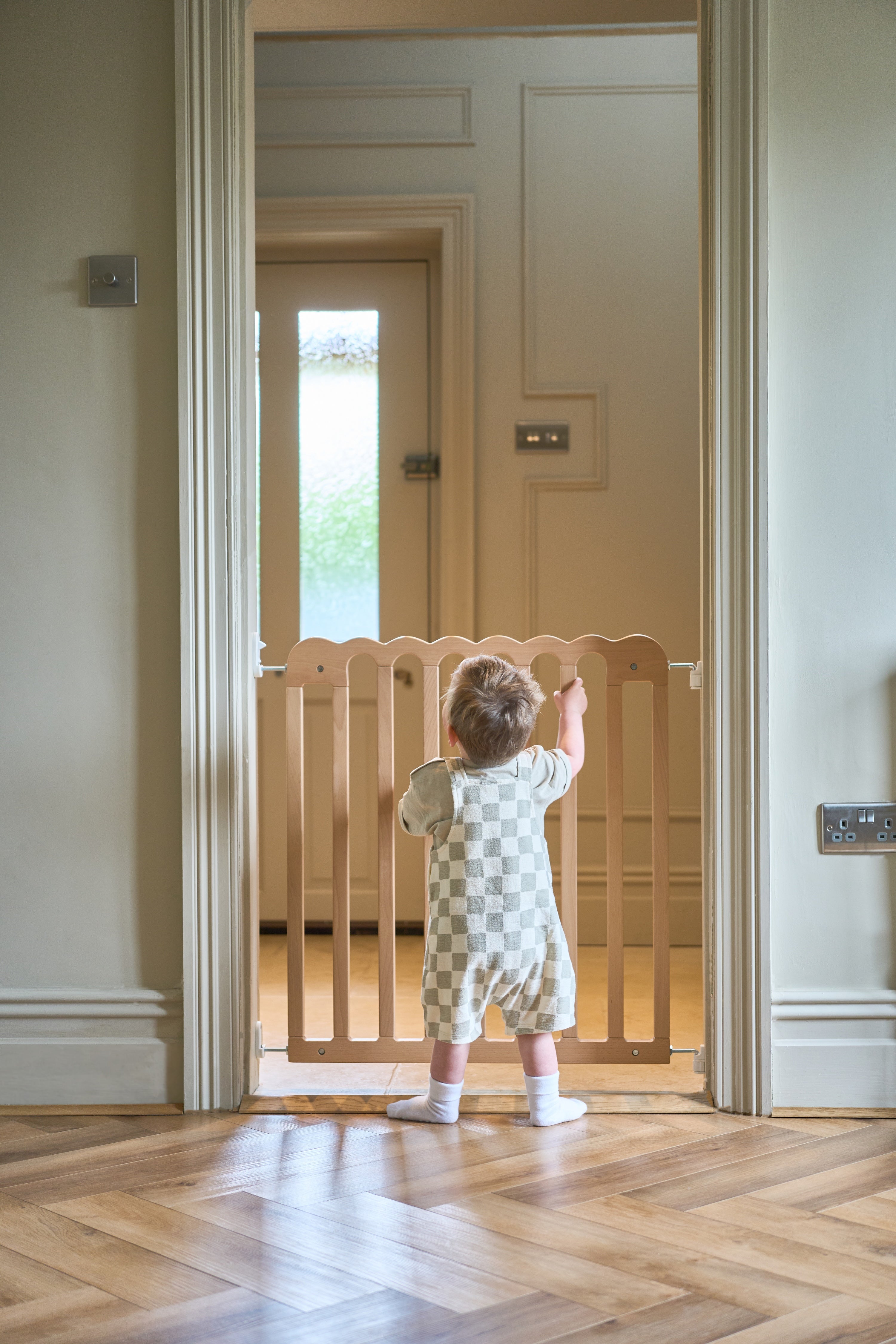 Child standing at a scalloped baby gate in a home setting