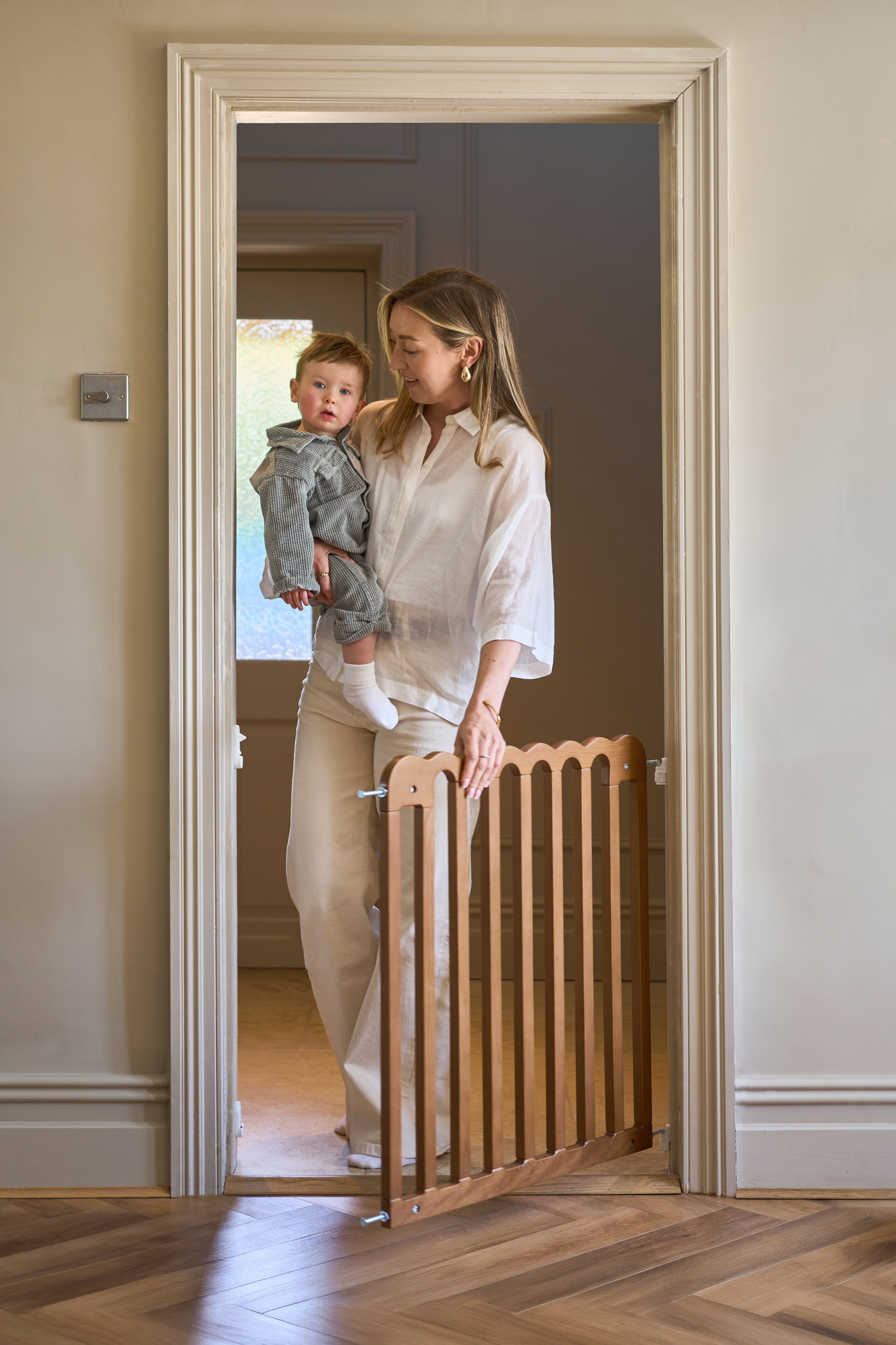 Woman holding a child next to a modern wooden baby gate in a home setting.